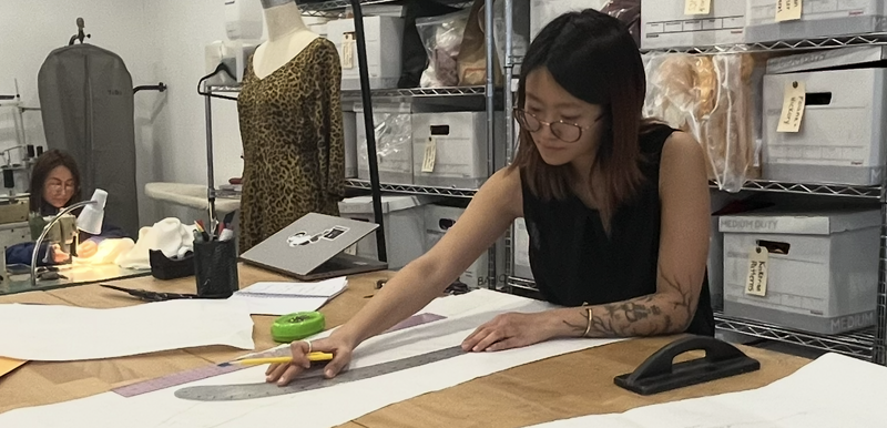 Thea working intently on the creating of a new garment pattern, with Sandra engaged in sample making in the background.